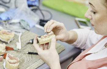 Person examining a dental mold and dentures at a workspace with tools.