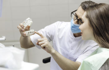 A dentist with a dental model explaining the pros of custom abutments to a woman in a dental chair.