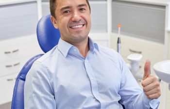 A satisfied man sitting in a dental chair showing his thumb up.