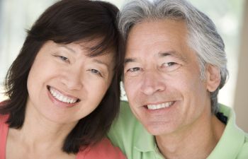 A smiling couple poses closely together, with the woman on the left and the man on the right.