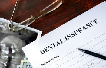Dental insurance form on a desk with a pair of glasses, a dental X-ray, and a pen.