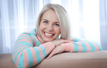 A smiling person with light hair leans on a cushion, wearing a striped pastel hoodie.
