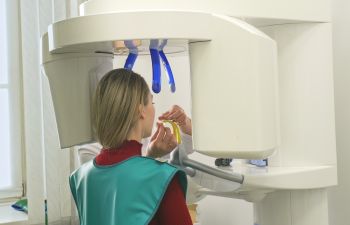 Person in a dental clinic undergoing a panoramic dental X-ray with protective apron and bite piece.