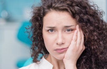 Person with curly hair holding their face, appearing to be in discomfort or pain, with a blurred blue background.
