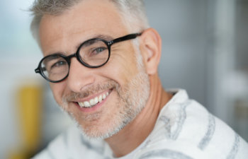Smiling man with glasses and gray hair, wearing a striped shirt, faces the camera.