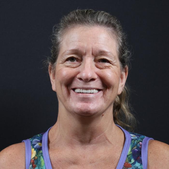 Woman smiling against a black background, wearing a floral tank top with purple trim.